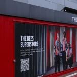 A Brentford Football Club merchandise kiosk promoting The Bees superstore with a QR code in London, United Kingdom.