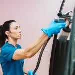 A beauty technician applying spray tan to a client inside a black booth.