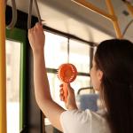 A young woman standing in a bus with a portable fan.