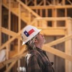 A construction worker wearing a hard hat with the Texas flag and looking up inside a wooden house construction site.