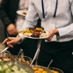 An employee holding up a plate of Mediterranean food from a catering event.
