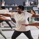 Focus on a black woman among a group doing aerobics together in a studio.