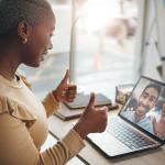 A black woman in an office happily putting two thumbs up during a video call.