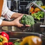 Person washing fresh vegetables over the sink.