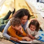 A mother reading a book to his young son and daughter on the floor.