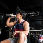 A young, fit man drinking water inside a gym.