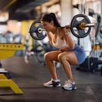 An athletic woman squatting with a barbell in a gym.