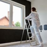 Woman in protective wear climbs a ladder to repaint a wall.