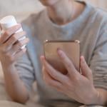 A person holding a vitamin bottle while checking prescription instructions in a smartphone.