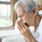 An elderly person blowing her nose after a sneeze.
