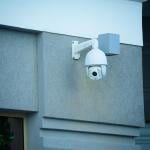 A view of a security camera on the facade of a gray building.