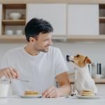 Man at home eating pancakes with his dog.