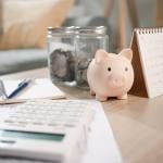 A piggy bank sits on a table with a calculator and a calendar.