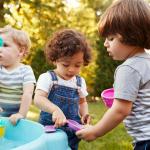Three little children playing around a water table in a garden.