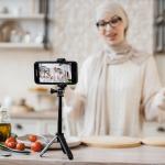 A young woman recording a video for her dieting and food blog using a smartphone on a tripod.