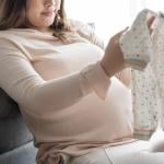 A pregnant woman checking on new baby clothes at home. 