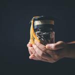 Person holding a jar of coins with a graduation cap as a concept of educational planning.