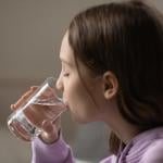 A young dehydrated teenage girl drinking a glass of water.