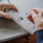 An elderly person arranging medicine in a pill box for the week.