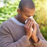 A young black man blowing nose outdoors due to allergy.