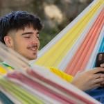 A happy young man in a hammock using his smartphone.