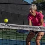 An elderly person enjoying a good time while playing pickleball in a court.