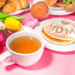 A pink-themed Mother's Day brunch meal featuring a bouquet of flowers, a cup of tea, and pancakes.