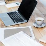 A workplace table with a laptop, coffee, and file documents.