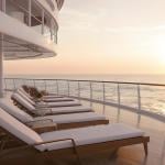 Lounge chairs on a ship deck facing the ocean's horizon during sunset.