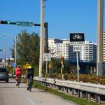Two cyclists travel north in a bike lane toward the Real Intracoastal Waterway Bridge in Florida, USA.
