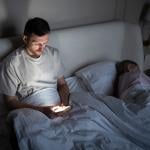 A man awake late at night and scrolling through his phone beside his asleep wife.
