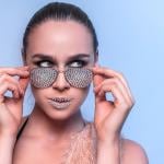 A female model wearing a rhinestone sunglasses and with rhinestones makeup on her lips.