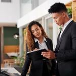 A pair of hotel receptionists checking their guest schedule on a digital tablet.