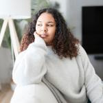 A pensive young woman sitting on the couch at home.
