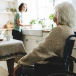 A selective focus shot of an elderly woman in a wheelchair looking at her caregiver at home.