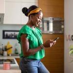 A happy black woman reading messages from smartphone at home.