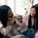 Two persons petting a cat while unpacking boxes in their new room.