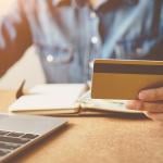 A person checking his credit card while reviewing finances from a laptop.