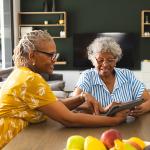 Two senior women sharing to use a tablet in their living room.