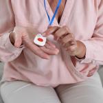 Woman pressing the button of a pendant medical alert system device at home.