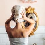 A person drying her hair in front of a mirror from a bathroom.