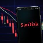 A smartphone displaying the SanDisk logo with a stock market graph in the background.
