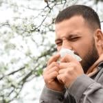 A person sneezing from an allergy outdoors. 