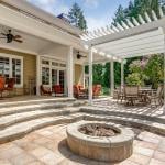 A modern luxury outdoor patio with a white pergola, fire pit, and outdoor sitting area.