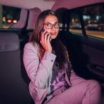 A young businesswoman in the backseat of a car late at night and talking on the phone.