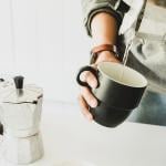 A person pouring hot water from a moka put to a cup before brewing coffee beans.