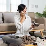 A young woman at home packing for a trip while talking to someone on the phone.