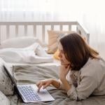 A parent working remotely from a bedroom while her baby toddler is sleeping in a crib.