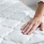 A person touching a bed's soft mattress. 