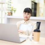 An employee thinking on a work-related matter while looking at a laptop from her office desk.